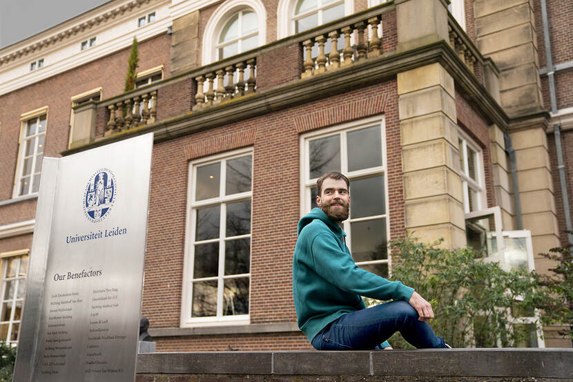 Jelmar Meester zit op een muurtje voor het gebouw van de Universiteit Leiden.