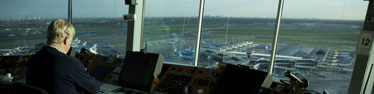 Luchtverkeersleider in verkeerstoren met op de achtergrond vliegtuigen aan gates
