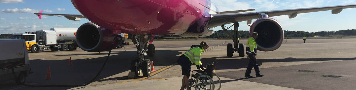 Vrouw duwt rolstoel met op de achtergrond een vliegtuig