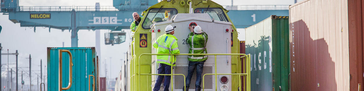 Drie mannen in beschermende hesjes inspecteren trein in havengebied