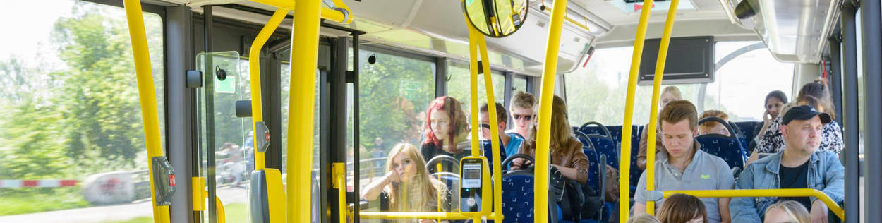 Een bus zit vol met voornamelijk jonge, passagiers. De een kijkt wat uit het raam en een ander op zijn telefoon.