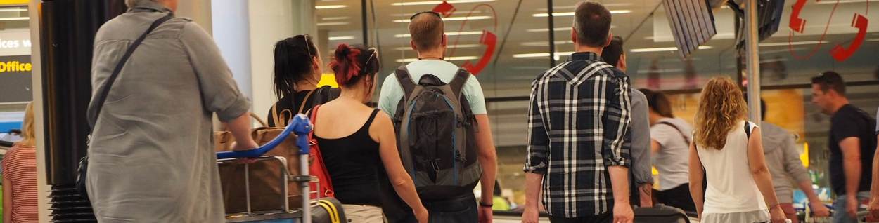 Diverse passagiers lopen in zomerse kledij door luchthaven Schiphol.