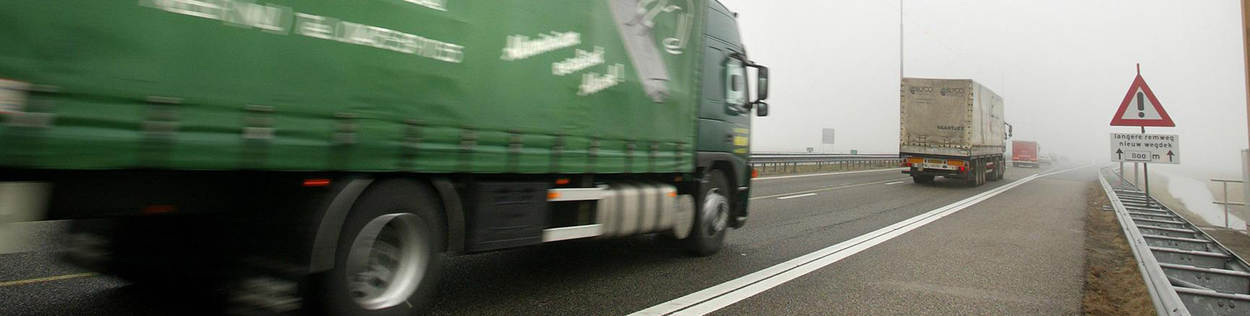 Een groene vrachtwagen rijdt in de mist over de snelweg.
