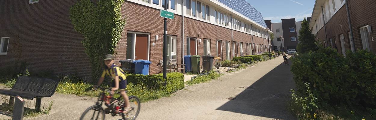 Een straat met doorzon huurwoningen. Op de voorgrond fietst een jongen.