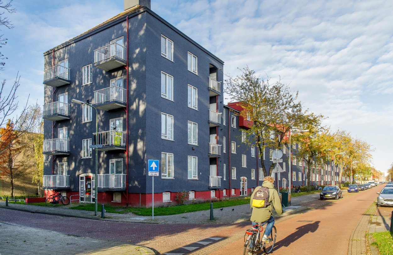Een straat met appartementen. Door de straat fietst een fietser.