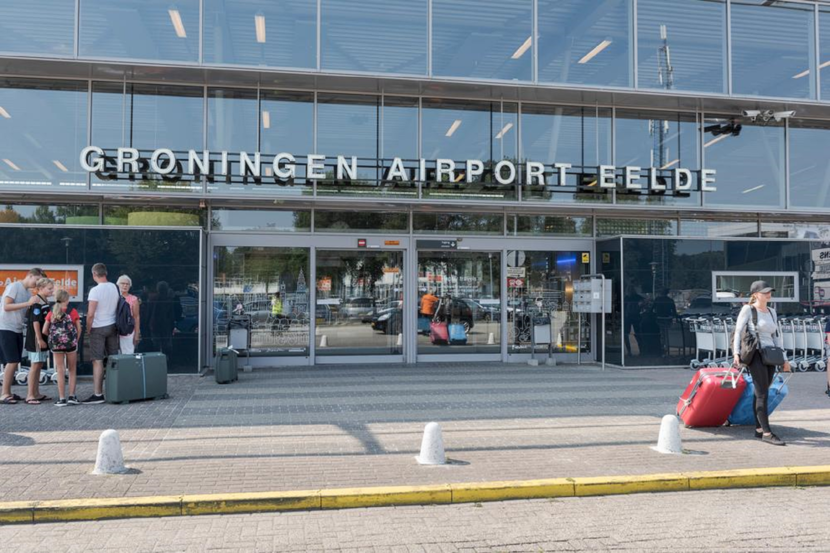 De entree van Groningen airport Eelde. Een aantal passagiers staan in zomerse kleding  op de stoep.