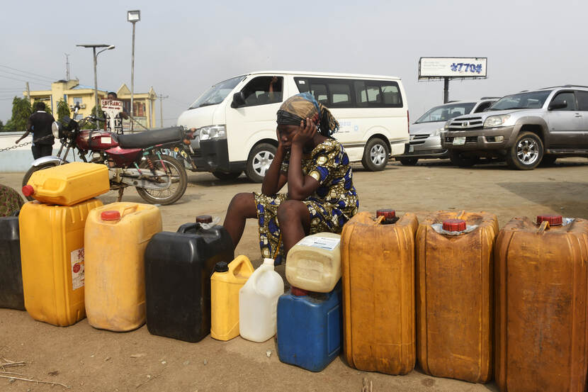 Afrikaanse vrouw zit naast een rij jerrycans voor benzine.