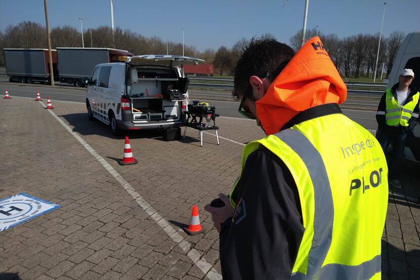 Controle van afvaltransporten op parkeerterrein naast de snelweg. Inspecteur bij zijn inspectiebusje treft voorbereidingen voor controles met drone.
