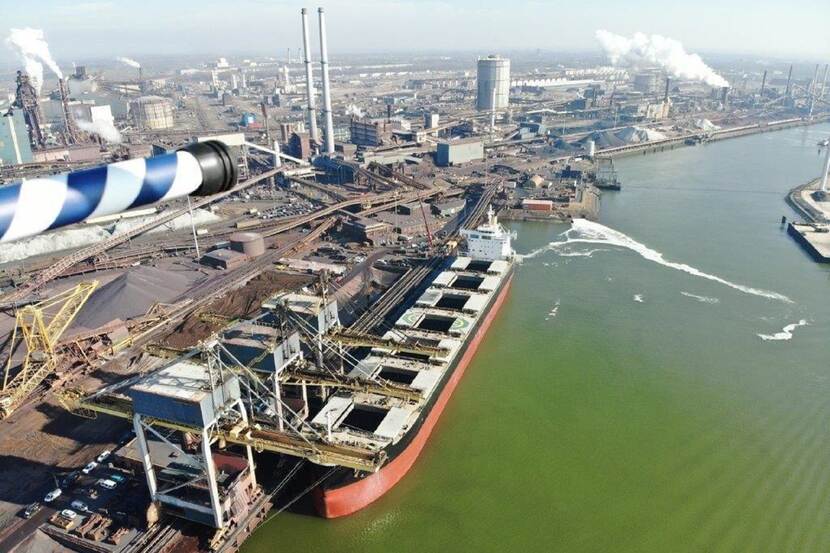 Foto vanuit vliegtuig van vrachtschip aan de kade bij het industrieterrein van Tata Steel in IJmuiden.