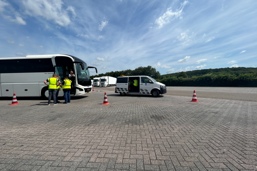 Inspecteurs controleren internationale passagiersbussen op parkeerplaats langs snelweg.