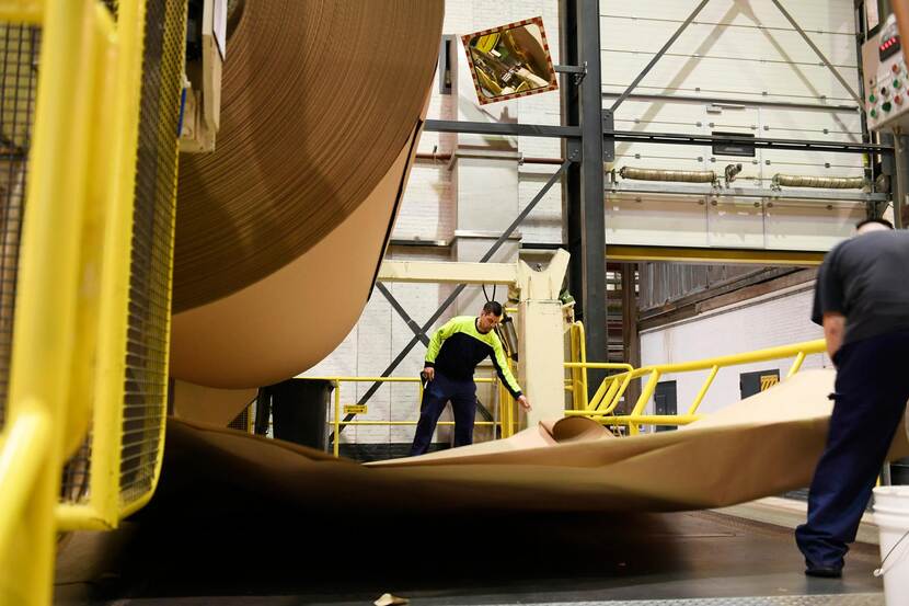 Twee medewerkers inspecteren een gigantische rol papier in een papierfabriek