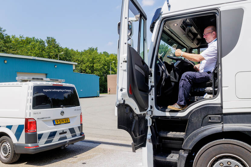 John Berkenbosch is inspecteur Goederenvervoer en zit in een vrachtwagen. Daar bekijkt hij gegevens. Voor de vrachtwagen staat een inspectie bus geparkeerd.