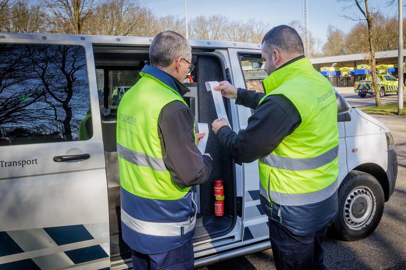 Michel Blox en John Kersten controleren tachograafgegevens terwijl ze naast een inspectie bus staan.