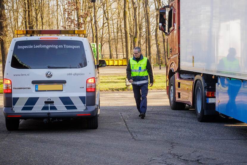 Michel Blox loopt over een parkeerplaats tussen een vrachtwagen en een inspectie bus.