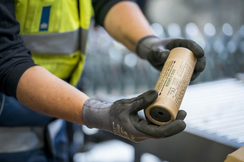 Een inspecteur met veiligheidshandschoenen houdt een stuk vuurwerk vast ter controle.