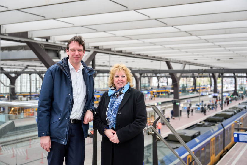 John Voppen en Karin Visser staan op een station. In de achtergrond is een trein te zien.